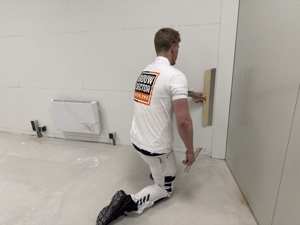 Stukadoor op zijn knieën strijkt het onderste deel van een muur glad