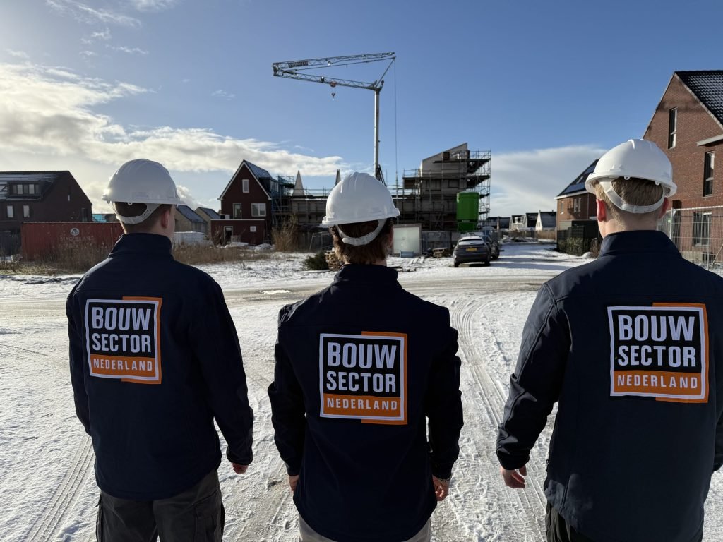 Drie vakmensen van Bouwsector Nederland met witte helm kijken naar een bouwplaats met kraan